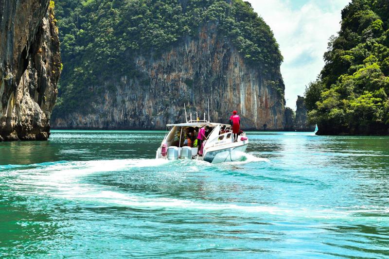 A high-speed boat cruising through the turquoise waters near James Bond Island, with dramatic limest