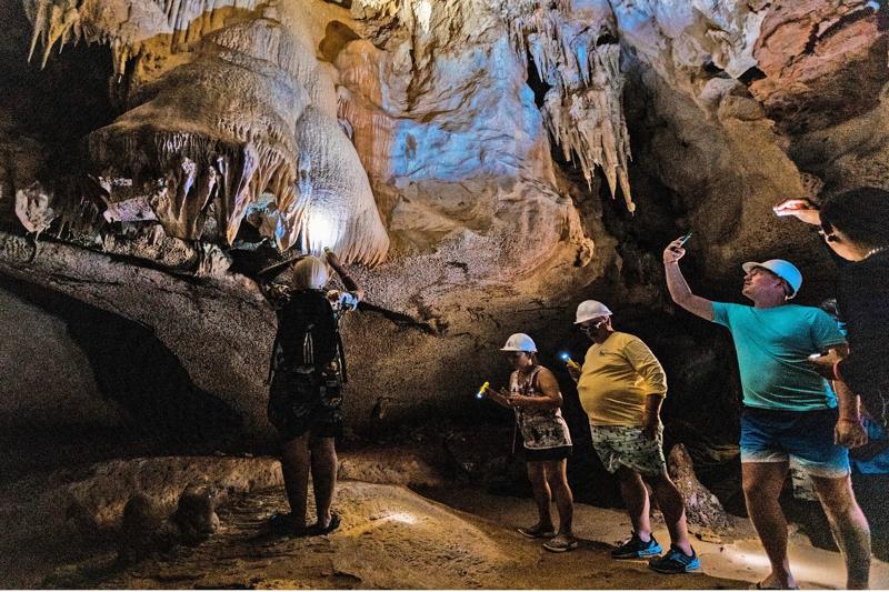 Cave exploration tour in Phuket with tourists observing stalactites and stalagmites.