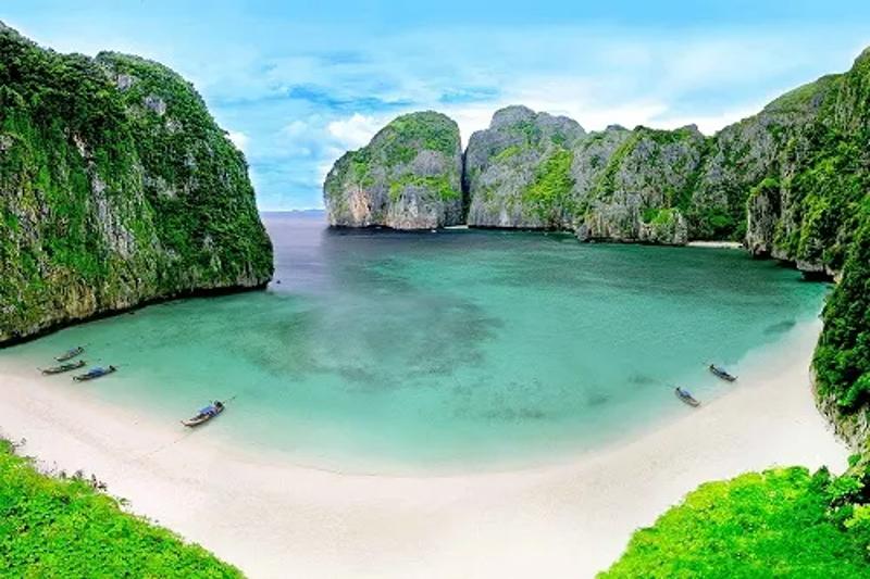 Clear waters and lush green cliffs at Phi Phi Islands with boats in the distance.