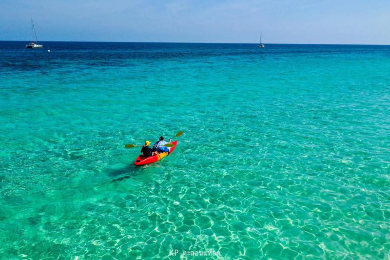 A vibrant kayak gliding through crystal clear water at Mai Ton Private Island in Thailand, with scen