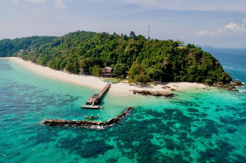 Tropical island paradise in Thailand featuring a wooden pier stretching into clear waters with a lus