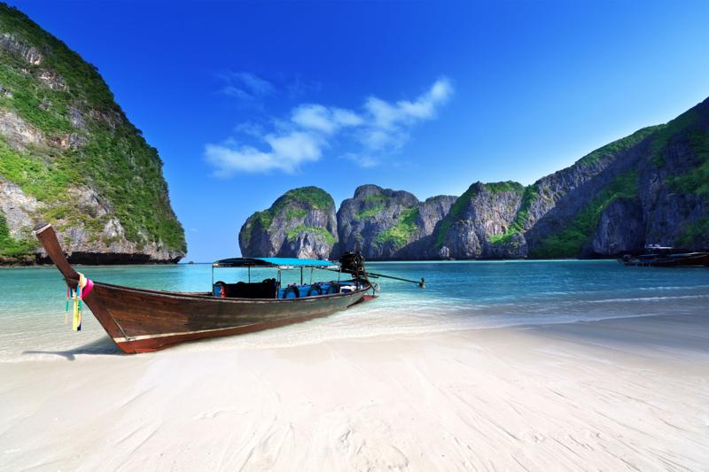 Traditional longtail boat on a tropical beach in Thailand, with crystal-clear waters and dramatic li
