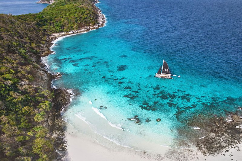 A traditional longtail boat anchored on a pristine beach in Thailand with turquoise water and lush h