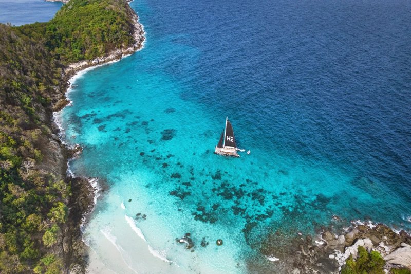 A luxury catamaran sailing through crystal-clear waters along a beautiful tropical coastline in Thai