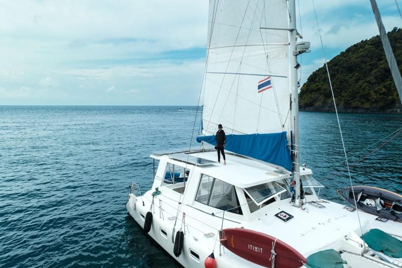 A catamaran boat sailing on the ocean with a person standing on the roof of the boat, with the ocean