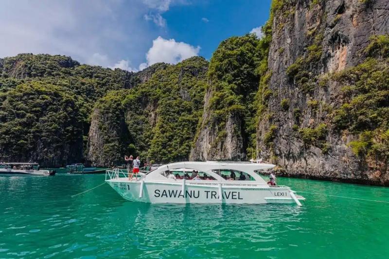 A Sawanu Travel catamaran named Lexi 1 docked near the dramatic cliffs of James Bond Island with cle