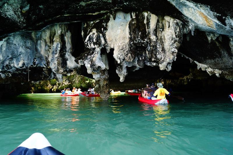 Tourists kayaking through caves in Phang Nga Bay, passing under rock formations and exploring the na