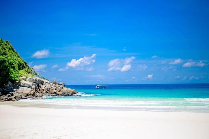 A speed Catamaran cruising through the turquoise waters near Khai Island, with dramatic cliffs in t