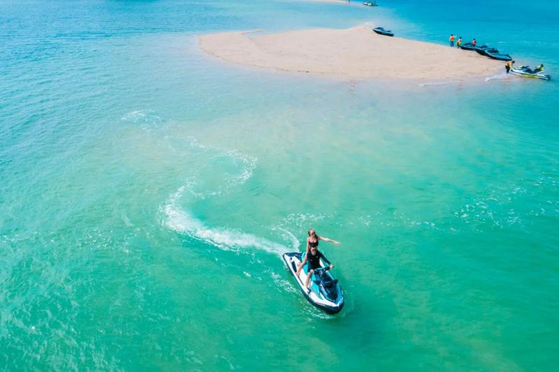 Several jet skis lined up on the beach with clear turquoise waters and a tropical landscape in Phuke